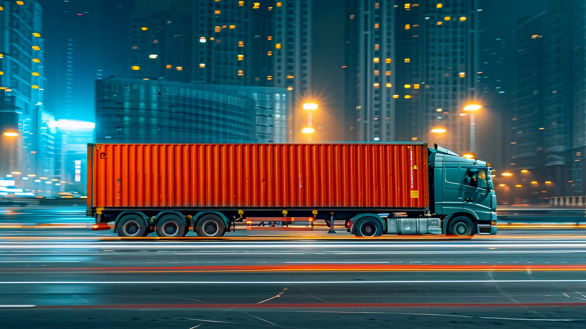 Red container truck in motion through lit urban area